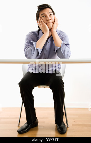 Giovani Asian business uomo seduto al banco fantasticando Foto Stock