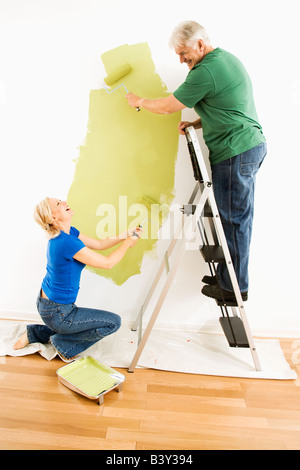 Coppia di mezza età pittura verde a parete con maschio sulla scaletta Foto Stock