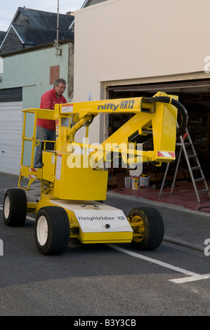 L'uomo operando un piccolo giallo motorizzato self drive cherry picker piattaforma sopraelevata per DIY sulla sua casa o home Foto Stock