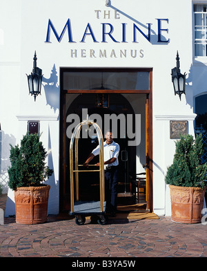 Sud Africa, Western Cape, Hermanus. Un portantino spinge il carrello bagagli attraverso l'entrata dell'Hotel. Foto Stock