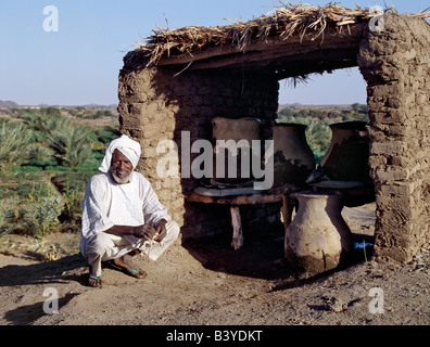 Sudan, Fiume Nilo, Quarta Cataratta. Un uomo Nubiano squat a fianco di coccio contenitori di acqua che mantenere acqua fresca nel calore del giorno. Il villaggio dove vive sul Fiume Nilo, vicino a Shaallal arraabia o la quarta cataratta, sarà allagato nel 2008 quando un enorme finanziato araba, cinese-costruzione della diga idroelettrica verrà completata. Già alcuni villaggi sono stati spostati in terre irrigate lontano. Foto Stock