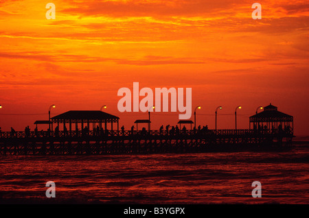 Il Perù, La Libertad, il sole tramonta sul Pacifico, scontornamento figure sul pontile a Huanchaco, sulla costa nord del Perù Foto Stock