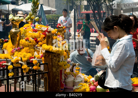 Una donna tailandese prega al Santuario di Erawan che offre bastoni di joss brucianti, ghirlande di fiori di marigold e cibo Foto Stock