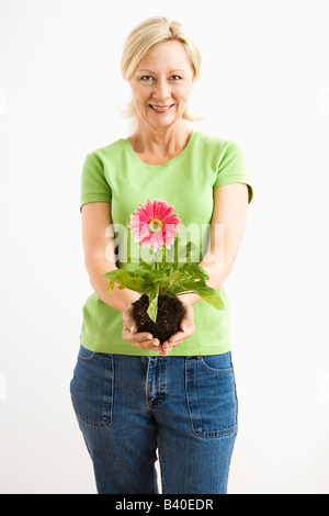 Ritratto di adulto sorridente donna bionda in piedi tenendo rosa gerber daisy impianto Foto Stock