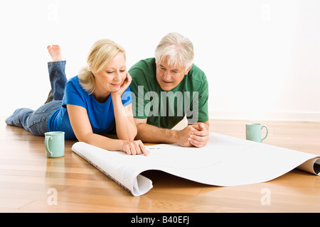 Coppia di mezza età che giace sul piano guardando gli schemi architetturali insieme Foto Stock