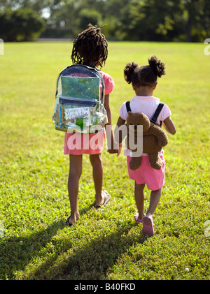 Due giovani ragazze che trasportano zaini andare a scuola a piedi nel parco di Chicago Foto Stock