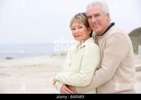 Matura in spiaggia abbracciando e sorridente Foto Stock