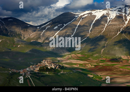 Il borgo di Castelluccio arroccato sopra il piano Grande con le montagne del Parco Nazionale dei Monti Sibillini, Umbria, Italia Foto Stock