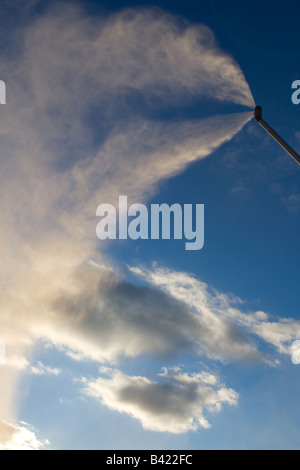 Un pennacchio di neve artificiale da impianti di innevamento programmato nelle Alpi Francesi, contro le nubi e cielo blu in background. Foto Stock