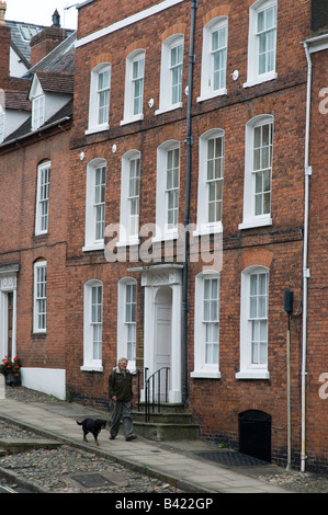 Uomo che cammina il suo cane nel passato di strada vecchia Regency era edifici in Broad Street Ludlow Shopshire England Regno Unito Foto Stock