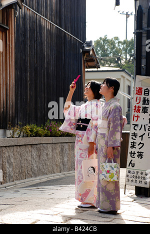 Due adolescenti ragazze giapponesi, vestiti in abiti tradizionali, scattare foto dei templi a Kyoto utilizzando un telefono cellulare Foto Stock