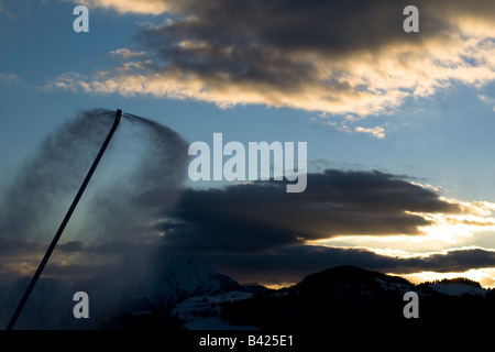 Un pennacchio di neve artificiale da impianti di innevamento programmato nelle Alpi Francesi, contro le montagne e le nuvole in background. Foto Stock