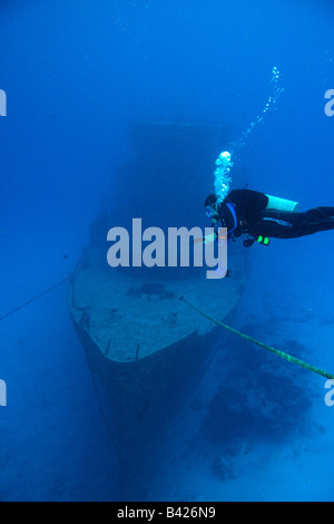 Un singolo subacqueo femmina di eseguire la decompressione di arresto di sicurezza con grande nave militare relitto in background. Foto Stock