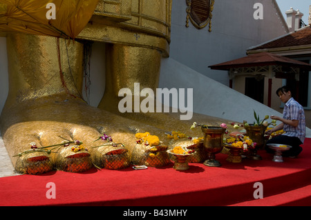 Una giovane donna tailandese che offre fiori di loto ai piedi della statua del Buddha alta 32 metri a Wat Indraviharn a Bangkok Thailandia Foto Stock