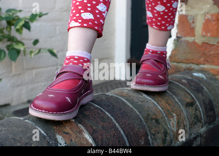 Ragazza giovane in equilibrio su una parete del giardino, indossando il nuovo red scarpe in pelle Foto Stock