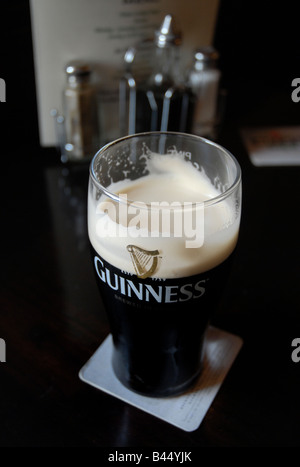 La pinta di Guinness Stout su un tavolo in un tipico pub inglese Foto Stock