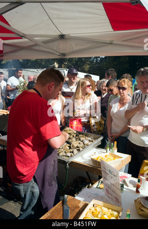 I clienti di accodamento guardare come un pescivendolo gusci di ostriche fresche all'aperto di stallo alimentare, Brighton, Inghilterra. Foto Stock