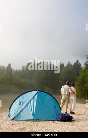 Matura in piedi accanto a una tenda a un fiume di montagna Foto Stock
