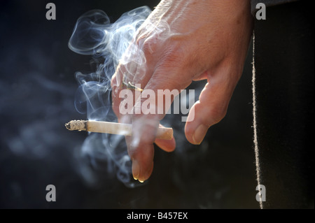 Un acceso il fumo di sigaretta in una mano WOMANS.RE salute sano stile di vita una malattia polmonare polmoni fumatori ospedali UK Cancer Foto Stock