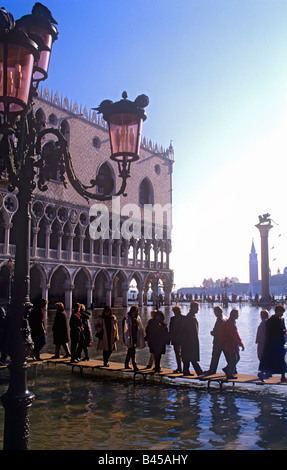 Venezia in alluvione. I visitatori a bordo di passeggiate in Piazza San Marco, lampade ornati in primo piano il Palazzo dei Dogi dietro a Venezia Italia Foto Stock