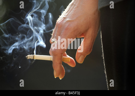Un acceso il fumo di sigaretta in una mano WOMANS.UK nuovamente problemi di salute malattia cancro il fumo passivo bruciare le dipendenze ETC REGNO UNITO Foto Stock