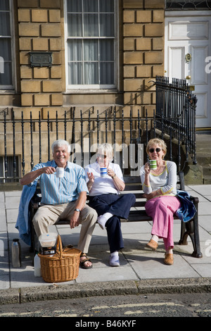 Le persone aventi un tè picnic sulla panchina in street Bath Regno Unito Foto Stock