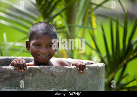 Ragazzo indiano giocando in un calcestruzzo rurale vasca di lavaggio. India Foto Stock