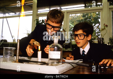 Due ragazzi che indossa gli occhiali di protezione calore un pezzo di roccia per una candela durante una scienza di classe a Manchester Scuola Grammer. Foto Stock