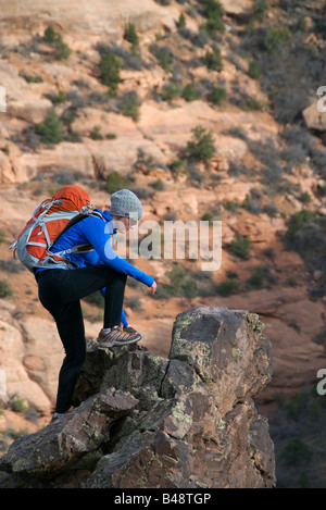 Una donna si arrampica ripida roccia arenaria con un pacco nel deserto di colorado Foto Stock