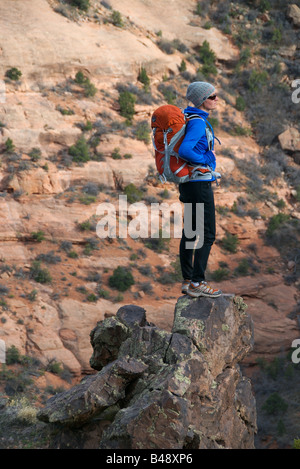 Una donna si arrampica ripida roccia arenaria con un pacco nel deserto di colorado Foto Stock