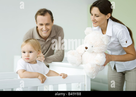 I genitori in piedi accanto al bambino nel presepe, madre holding Teddy bear, Il bambino che guarda lontano Foto Stock