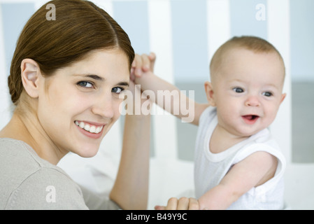 La madre tiene il bambino con le mani in mano e sorridente in telecamera Foto Stock
