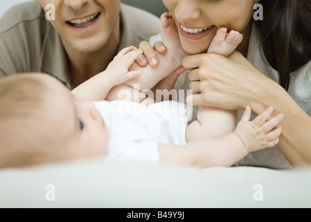 I genitori sorridente giù a baby, azienda madre del bambino in piedi, vista ritagliata Foto Stock