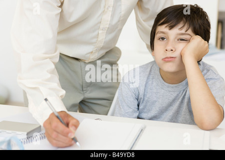 Padre aiutando figlio con i compiti, ragazzo tenendo la testa e lo sguardo lontano, vista ritagliata Foto Stock