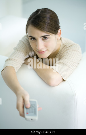 Donna appoggiata sul lato del lettino, puntando il telecomando, sorridente in telecamera Foto Stock