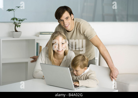 Famiglia riunita intorno al computer portatile, little boy digitando, genitori sorridente in telecamera Foto Stock