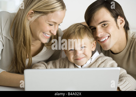 Famiglia riunita intorno al computer portatile, padre e figlio sorridente in telecamera Foto Stock