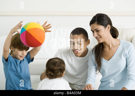 Famiglia riunita intorno a toddler girl, sorridente, ragazzo gettando palla in aria Foto Stock