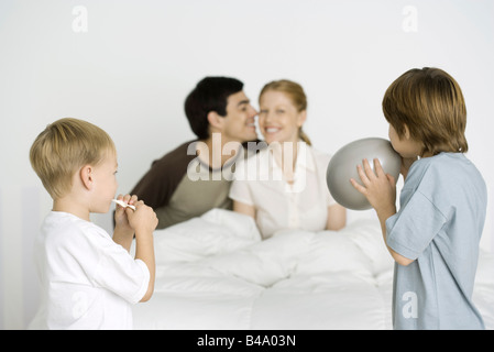 Due ragazzi gonfiare palloncini, genitori sorridente sul letto in background Foto Stock