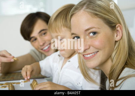 Famiglia giocare gioco di bordo, madre sorridente in telecamera Foto Stock