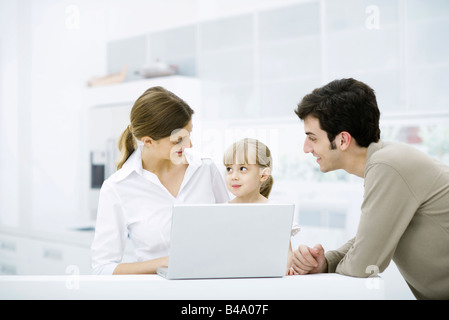 Famiglia riunita intorno al computer portatile, sorridente, ragazza guardando madre Foto Stock