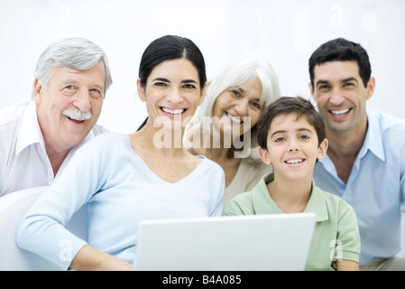 Multi-generazione famiglia riunita intorno al computer portatile, sorridente in telecamera Foto Stock