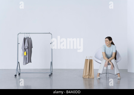 Donna seduta con le borse della spesa, guardando il tee-shirts su rack nelle vicinanze Foto Stock