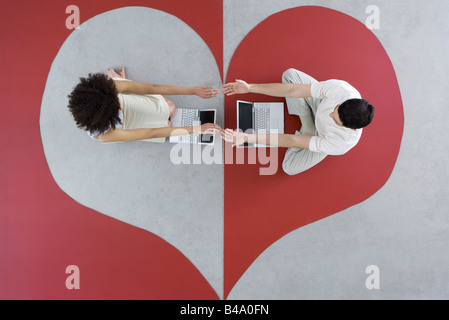 L uomo e la donna seduta con i laptop sul grande cuore, braccia, toccando le mani, vista aerea Foto Stock