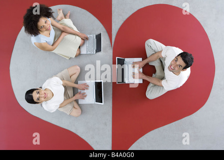 Due donne e un uomo seduto su un grande cuore, utilizzando computer portatili, sorridente fino alla fotocamera Foto Stock