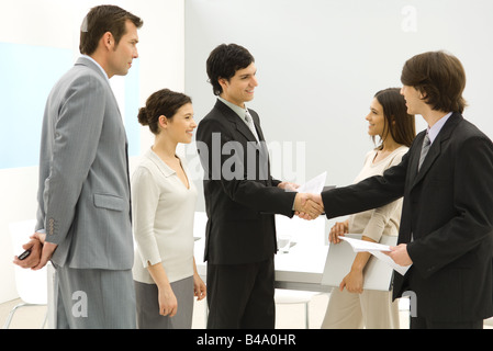 Business Associates incontro, stringono le mani mentre gli altri stanno a guardare Foto Stock