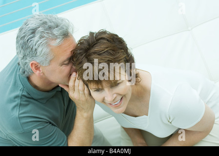 Donna guarda lontano sorridente come suo marito sussurra nel suo orecchio Foto Stock
