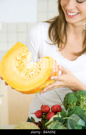 Donna che mantiene grande fetta di zucca raw, sorridente Foto Stock