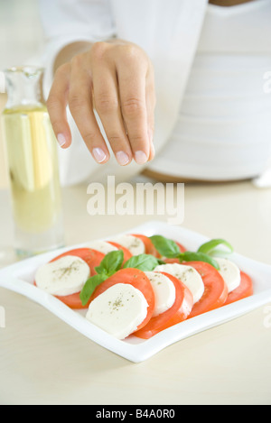 Donna preparazione piatto di insalata caprese, spolverata di pepe Foto Stock