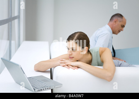 Giovane donna rilassante sul divano, utilizzando il computer portatile, imprenditore lettura in background Foto Stock